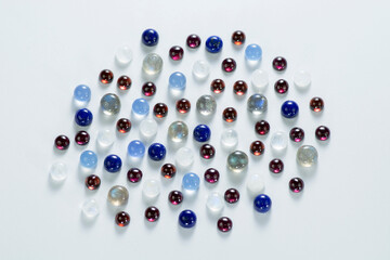 Lot of natural cabochon round polished gemstones. Lavender chlcadony, blue lapis lazuli, labradorite, rainbow moonstones and red rhodolite garnet stones group. View from above. White background.
