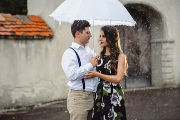 Loving happy couple, man and woman walking in the rain of city streets. Girl and guy kissing under white umbrella when it is raining, closeup.
