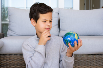Young pensive boy holding planet earth in his hands at home