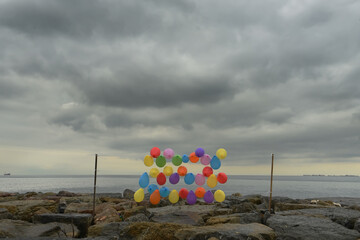 Bright airy balls of different colors on the rocky shore overlooking the gloomy sky and sea.