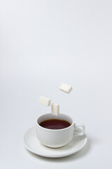 Sugar cubes fall into a cup of tea on a white background. A cup of tea with refined sugar. Tea time