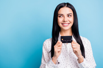 Photo of young attractive woman happy positive smile hold credit card dream look empty space isolated over blue color background
