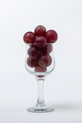 Pink grapes in a wine glass on a light background. Large pink grapes on white background