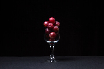 Pink grapes in a wine glass on a dark background. Large pink grapes on black background