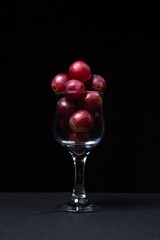 Pink grapes in a wine glass on a dark background. Large pink grapes on black background