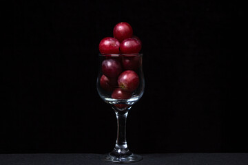 Pink grapes in a wine glass on a dark background. Large pink grapes on black background