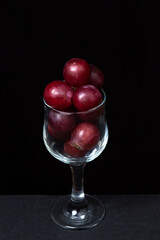 Pink grapes in a wine glass on a dark background. Large pink grapes on black background