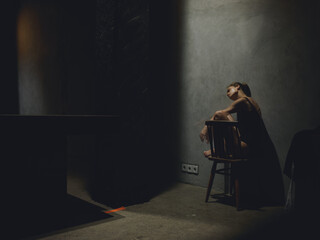 sad woman sitting on a high chair indoors leaning against the wall dark room silhouette interior