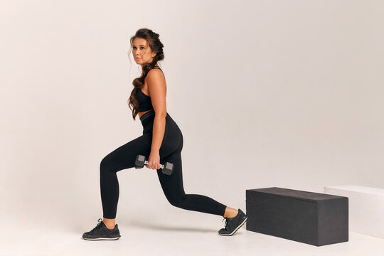 Athletic young woman in a black suit lunges forward with dumbbells on a white background. crossfit. fitness squats healthy lifestyle