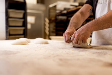 Fototapeta na wymiar hands of bread baker kneading fresh and uncooked bread dough on table during bread preparation process in bakery house. concept of manual bread making