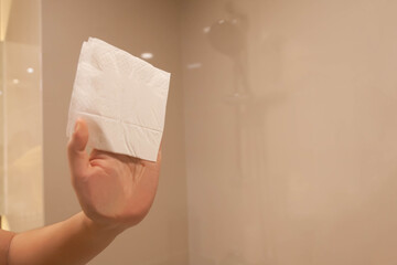 Hand holding tissue wipes cleaning glass surface in bathroom. Selective focus on some part of tissue. Copy space
