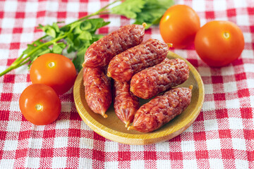 raw smoked mini sausages in a wooden plate on a red checkered towel