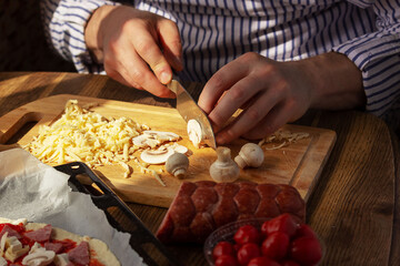 A man prepares pizza at home, cuts the ingredients, selective focus.