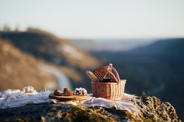 Picnic on the rocky mountain. Basket with wine and baguette and wooden tray with croissants.