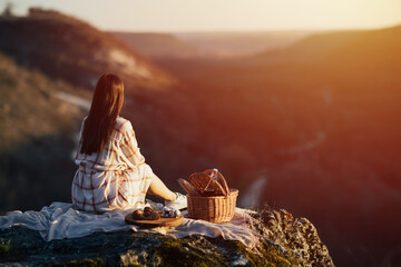 Young woman in tender dress is having picnic in the mountains sit with their backs to the camera,...