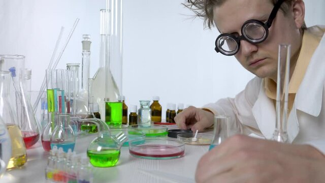 funny scientist between flasks and reagents. laboratory assistant in big glasses, a robe, shaggy. passionate about his work, science
