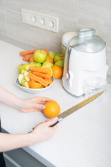 Girl prepares homemade fresh juice made with apples, oranges and carrots. Vertical photo.