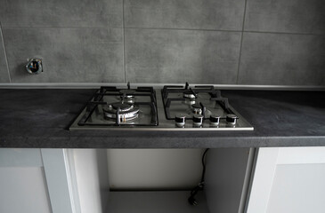 Stainless grey metal kitchen gas stove installed on a the kitchen with a dark grey table top.