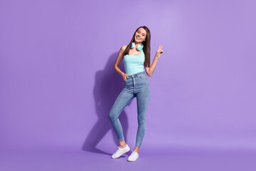 Full length body size photo of girl wearing headphones showing v-sign gesture smiling isolated on pastel violet color background