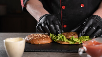 step by step recipe. Stage 4. The chef prepares a delicious burger. Close-up of a hand in black gloves putting a cutlet on a green leaf of lettuce, menu, delicious and unhealthy food.