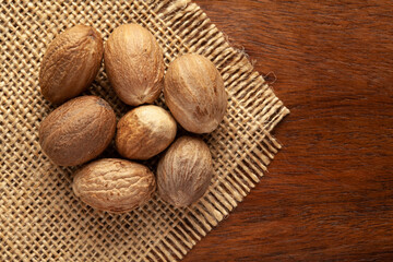 Macro close-up of Organic nutmeg seed  (Myristica fragrans) on the wooden top background and jute mat. Pile of Indian Aromatic Spice. Top view