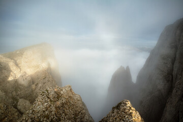 Top of the mountains. High sharp rocks in the fog at sunset. Colorful nature background