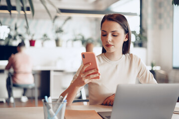 Young attractive businesswoman using her smartphone in office