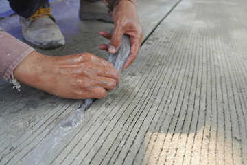 Workers hand is dripping sealant to cover crack in the concrete floor at construction site.