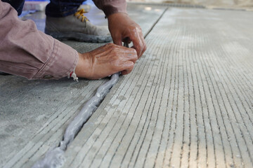 Workers hand is dripping sealant to cover crack in the concrete floor at construction site.