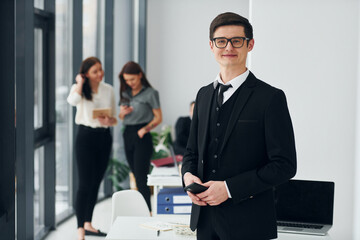 Young man with phone. Group of people in official formal clothes that is indoors in the office