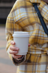 A cup of coffee in a disposable cup in the hands of a stylish woman in the city. Cup design mockup