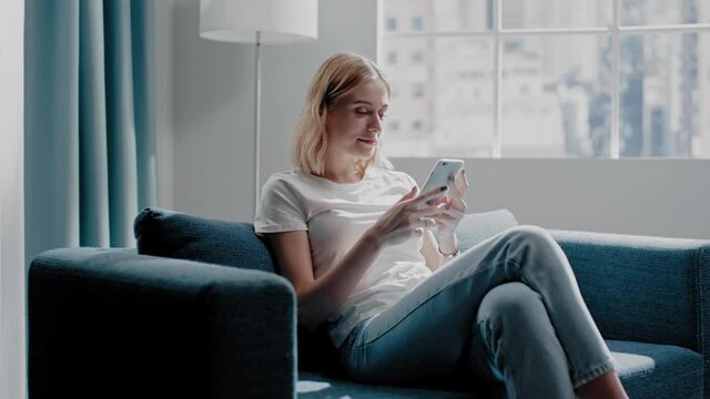 Woman looks at picture on phone sitting on azure sofa
