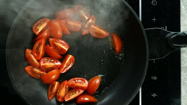 Preparation fried eggs with tomato in frying pan for breakfast on electric stove on domestic kitchen. Raw broken chicken egg falls into hot skillet. Top view. Top down food. Close-up.
