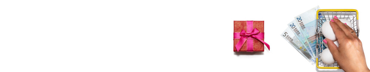 Basket full of fresh white eggs with euro bills underneath it nex to red gift box with purple ribbon. Top view. Isolated on white background. Eggs shopping, discount concepts. Banner size. Copy space