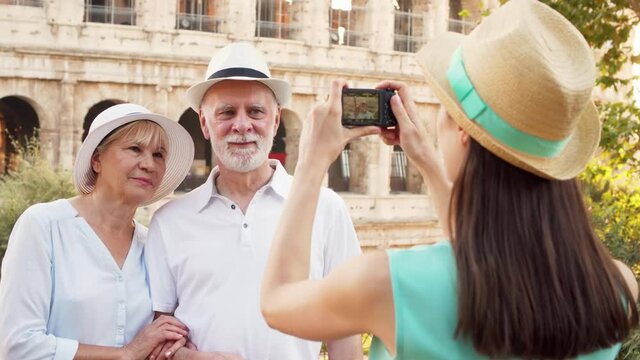 Family of travelers on vacation in Rome. Seniors and daughter take photo on camera near Colosseum