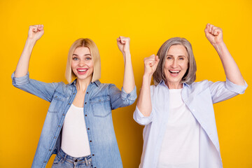 Photo portrait of mother and daughter laughing gesturing like winner isolated vibrant yellow color...