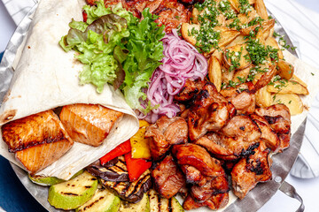 Mixed grill meat fried vegetables and grilled salmon fish fillets decoration in warm dish. Assorted delicious grilled kebab served with herbs on platter. Restaurant menu barbecue plate Bbq party meal