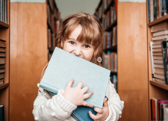 Baby girl in the library with books in her hands. cute toddler explores the bookshelves