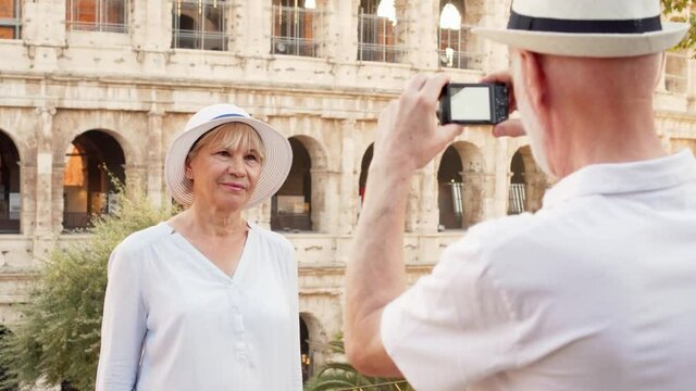 Family of senior travelers enjoy vacation in Rome. Senior couple make photo on camera near Colosseum