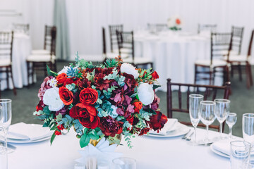 Fancy table set for dinner with flower composition in restaurant, luxury interior background. Wedding elegant banquet decoration and items for food arranged by catering service on white table.