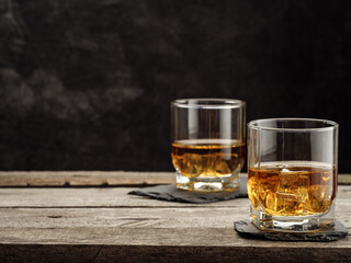 Two glasses of whiskey stand on an old wooden table. Copy space.