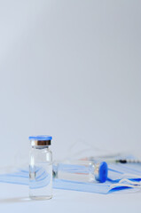 Creative ideas of vaccination concept. Top view of syringe with medical masks and vaccine vial glass bottles for vaccination against COVID-19. Coronavirus pandemic. Copy space. 