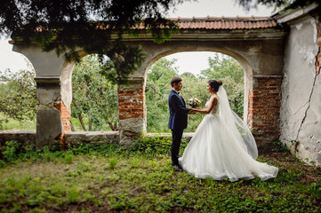 Beautiful wedding couple holding each other's hands, posing in front of an old destroyed estate.