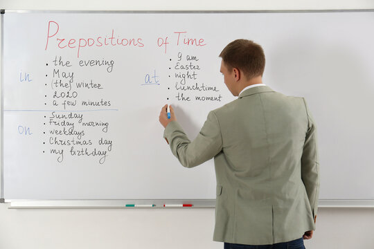 English teacher giving lesson on prepositions of time near whiteboard in classroom, back view