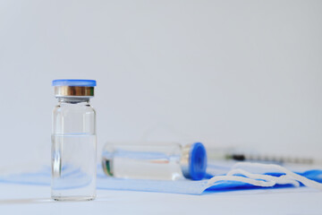 Creative ideas of vaccination concept. Top view of syringe with medical masks and vaccine vial glass bottles for vaccination against COVID-19. Coronavirus pandemic. Copy space. 