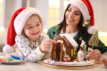 Mother and daughter decorating gingerbread house at table indoors