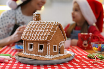 Mother and daughter in Santa hats cooking together, focus on gingerbread house