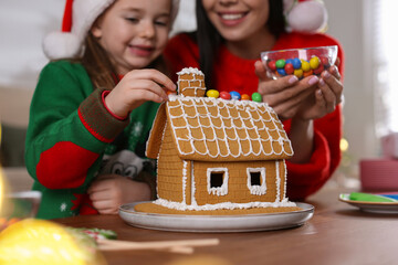 Mother and daughter decorating gingerbread house at table indoors, closeup