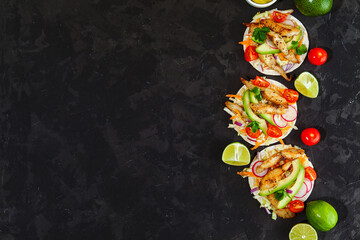 Fototapeta na wymiar Tacos with crispy fish, avocado, guacamole sauce and lime on dark background. Top view with copy space. Mexican cuisine