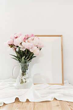 Vertical frame mockup on a wooden table in the kitchen. Glass vase with a bouquet of pink peonies. Scandinavian style interior.